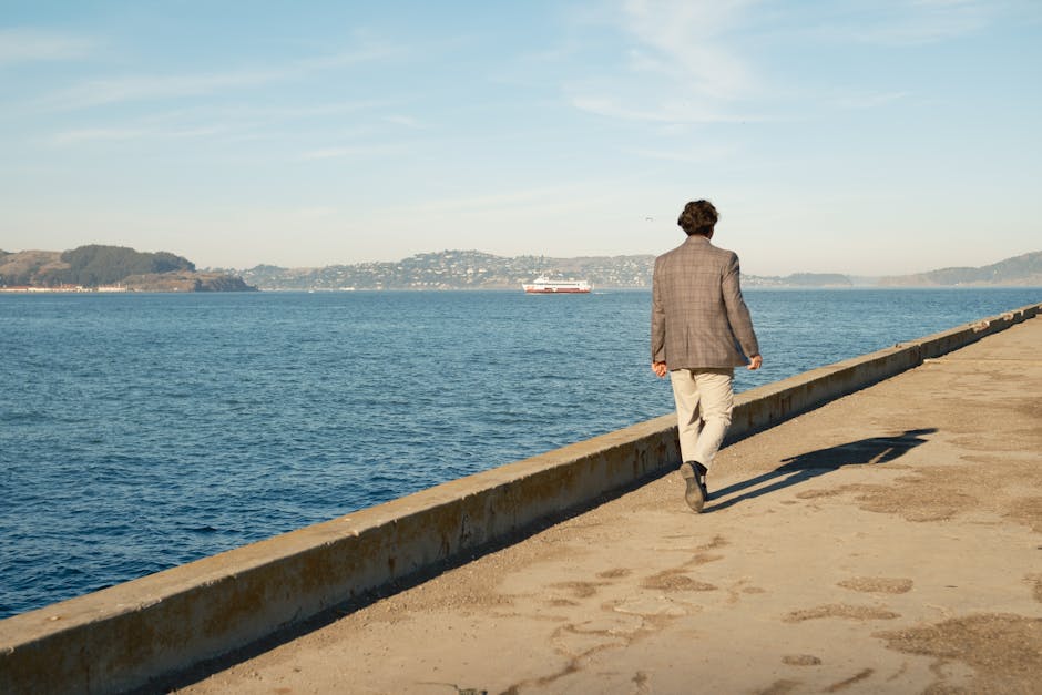 A man in a suit walks along a pier by the ocean in Los Angeles under a clear blue sky