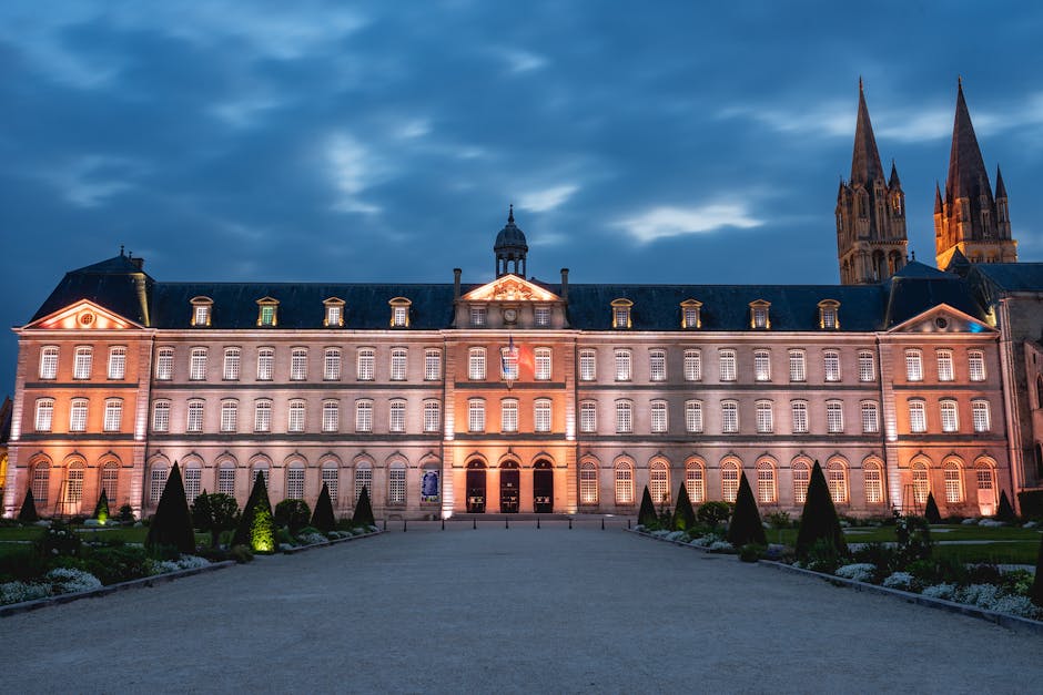Illuminated facade of a historic abbey at dusk in Caen, Normandy, France. A landmark sight for travelers