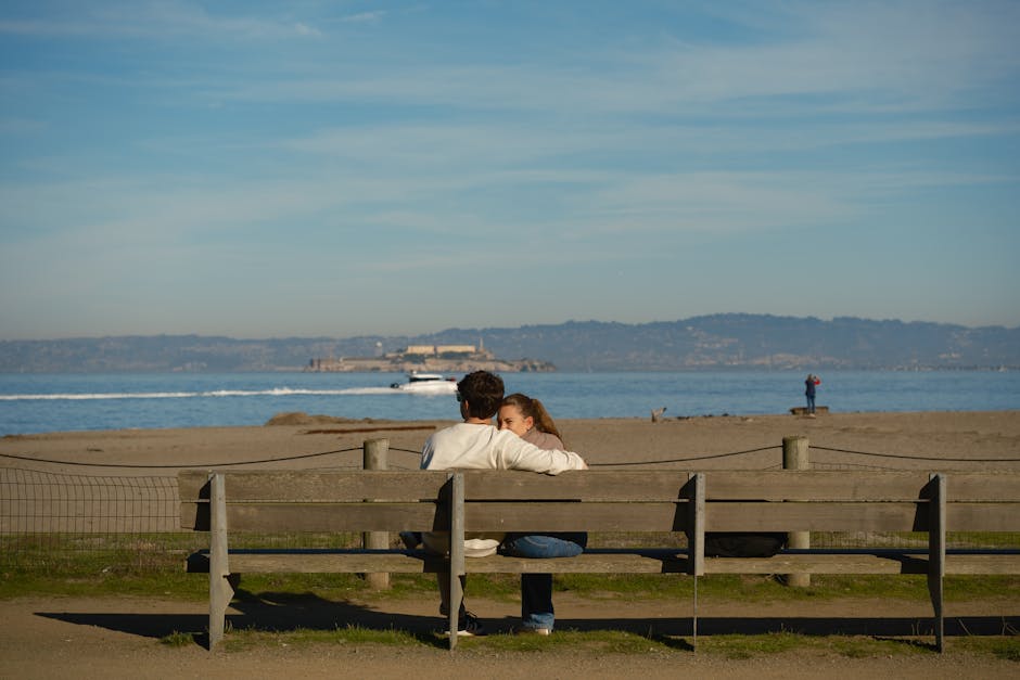 A romantic couple enjoys a serene moment on a beachfront bench with an ocean view in Los Angeles.