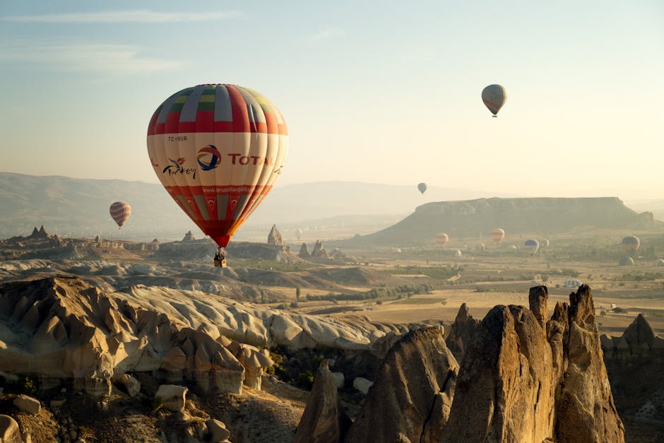 Breathtaking aerial view of hot air balloons floating over Cappadocia's unique rock formations at sunrise.