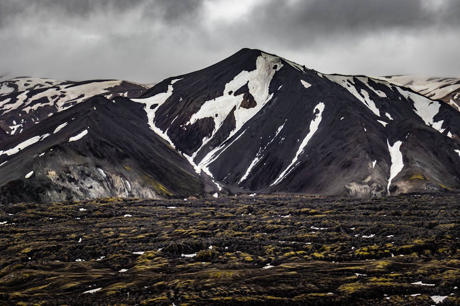 A mesmerizing view of Iceland's volcanic mountains with patches of snow and lush moss-covered lava fields.